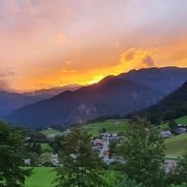 Eine malerische Ansicht eines Tals mit einem Sonnenuntergang über den Bergen und einem kleinen Dorf im Vordergrund.