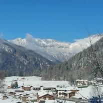 Ein malerisches Dorf in einem verschneiten Tal, umgeben von hohen Bergen unter einem klaren blauen Himmel.