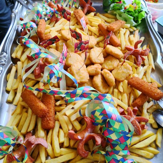 Ein Tablett mit goldenen Pommes Frites, Nuggets und Würstchen, geschmückt mit bunten Bändern und Flaggen.