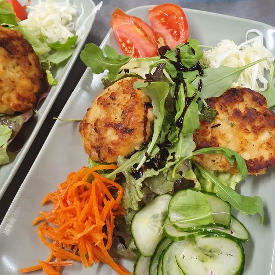 Zwei weiße Teller mit Salat, bestehend aus Salat, Gurken, Karotten und Tomaten, sowie zwei knusprigen Hähnchenschnitzeln mit Soße.