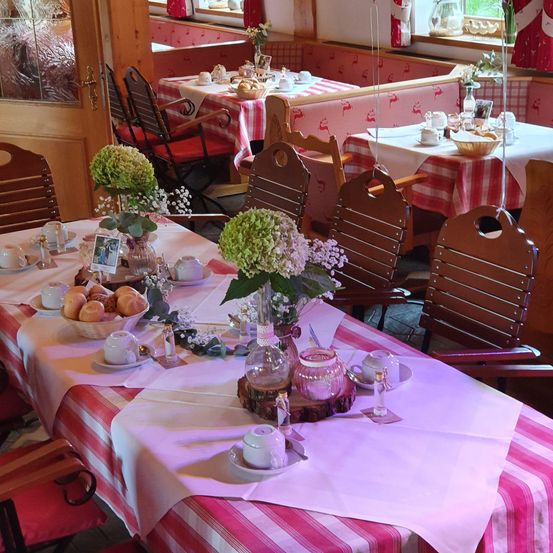 Ein Esszimmer mit einem Tisch für das Frühstück gedeckt mit Brot, Gebäck, Blumen und Tee. Im Hintergrund sind zwei weitere Tische mit Luftballons gedeckt.