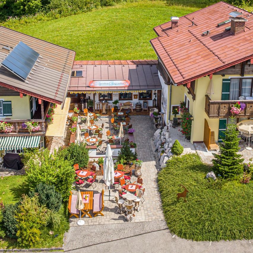 Ein Luftbild eines ländlichen Resorts mit zwei Häusern, einem Restaurant und Sitzgelegenheiten im Freien. Die Häuser haben rote Dächer und Solarpanels. Bäume und Berge sind im Hintergrund.