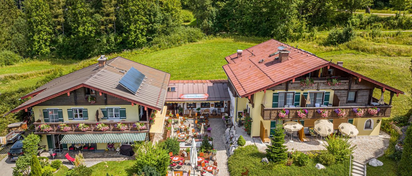 Ein Luftbild eines ländlichen Resorts mit zwei Häusern, einem Restaurant und Sitzgelegenheiten im Freien. Die Häuser haben rote Dächer und Solarpanels. Bäume und Berge sind im Hintergrund.