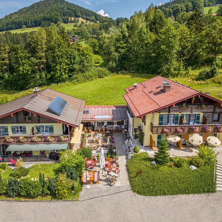 Ein Luftbild eines ländlichen Resorts mit zwei Häusern, einem Restaurant und Sitzgelegenheiten im Freien. Die Häuser haben rote Dächer und Solarpanels. Bäume und Berge sind im Hintergrund.