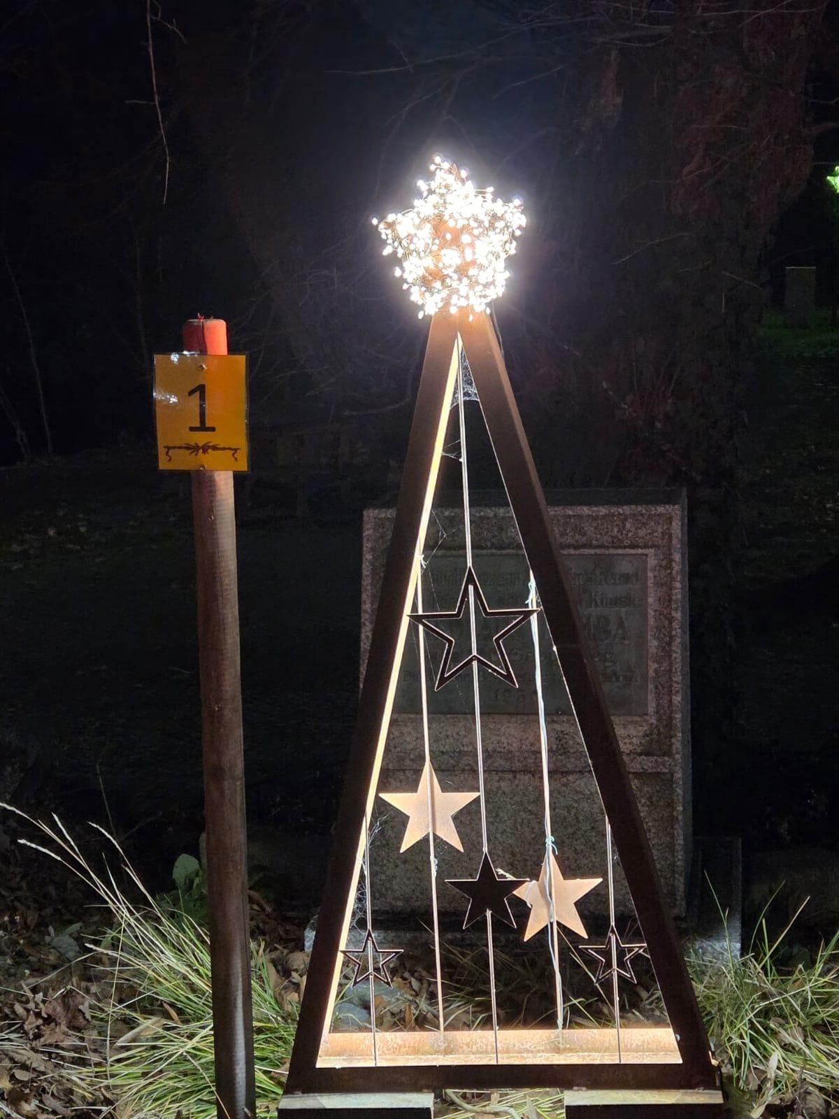 Ein beleuchteter Weihnachtsbaum mit Sternendekorationen ist nachts zu sehen. Ein gelbes Schild mit der Nummer eins ist an einem Pfosten sichtbar.