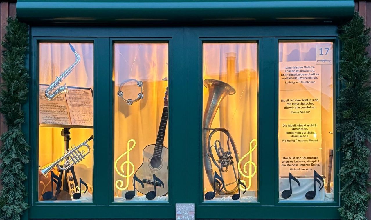 Ein Schaufenster zeigt Musikinstrumente wie Trompete, Gitarre und Tuba, beleuchtet von Neonlichtern. Das Fenster hat auch deutschen Text über Musik.