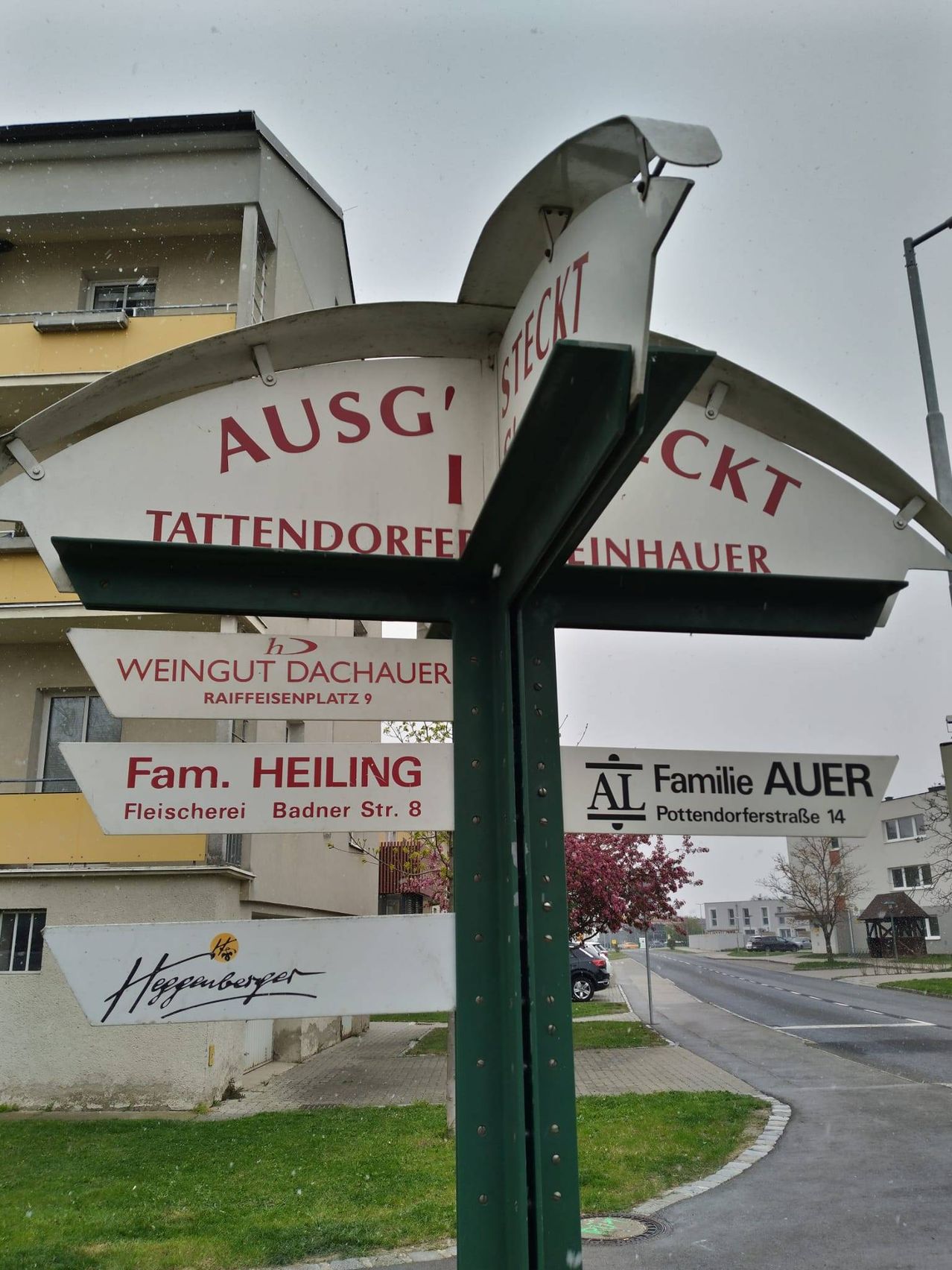 Ein Straßenschild zeigt Namen von Betrieben und Straßen, darunter Ausg' Tattendorf, Steck, Weingut Dachauer, Fam. Heiling und Familie Auer.