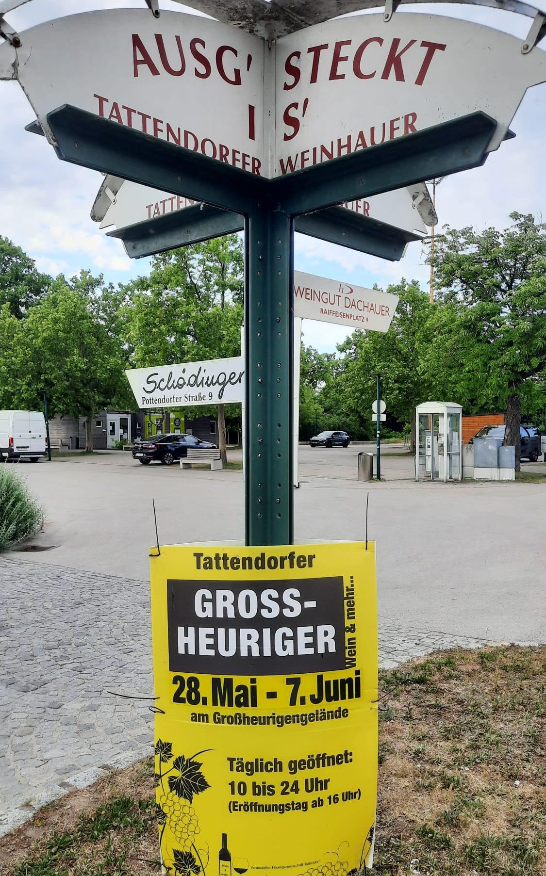 Ein Schild, das ein Weinfest in Deutschland ankündigt, gibt ein Groß-Heuriger-Event an. Das Plakat zeigt 'Gross-Heuriger' und die Daten vom 28. Mai bis 7. Juni an.