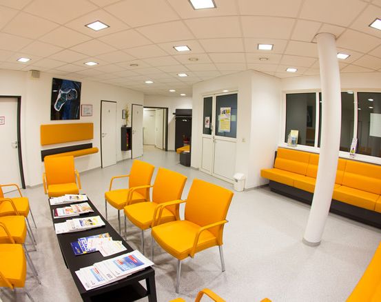 Ein Wartezimmer mit gelben Stühlen, einem Schreibtisch mit Papieren und einer großen Säule.