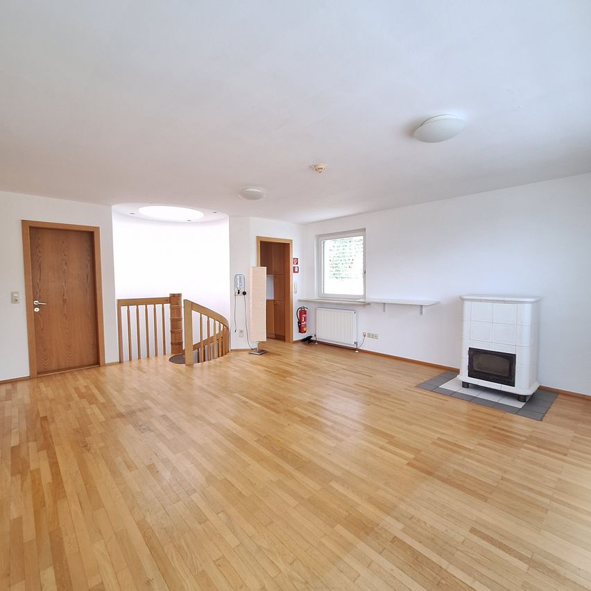 Ein leerer Raum mit Holzböden, weißen Wänden und einer Wendeltreppe. Ein weißer Kamin steht rechts und ein Feuerlöscher ist an der Wand montiert.