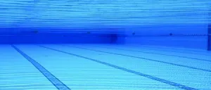 Ein Schwimmbecken mit blauem Wasser und Bahnlinien. Das Becken ist leer und mit blauen Lichtern beleuchtet.