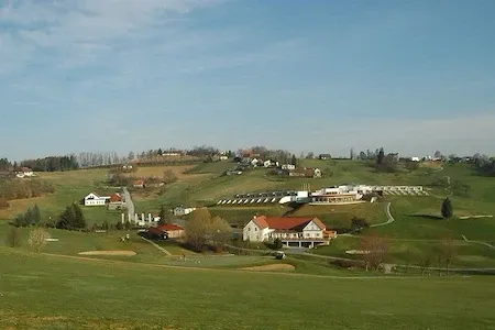 Eine Luftaufnahme eines Golfplatzes mit Häusern und Bäumen. Die Häuser befinden sich auf der rechten Seite, und im Vordergrund befinden sich Golflöcher.