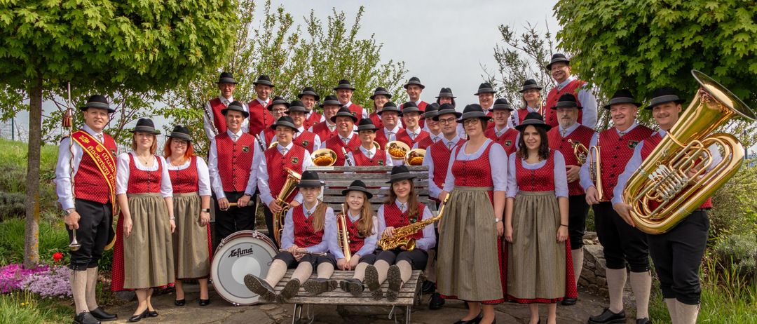 Eine Gruppe von Menschen in traditioneller deutscher Kleidung, einschließlich Hüten und roten Westen, posiert für ein Foto. Sie halten Musikinstrumente.