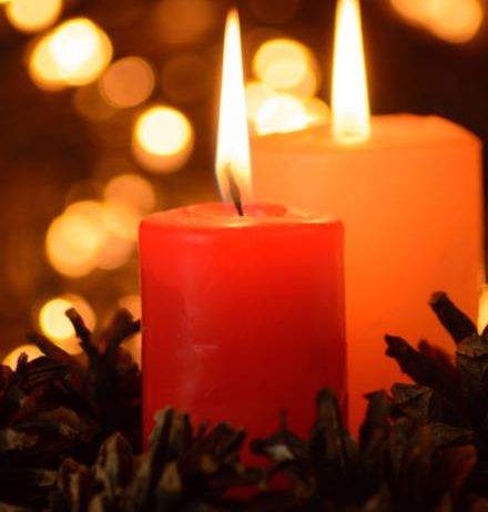 Zwei rote und orange Kerzen brennen in einem Kranz aus Tannenzapfen und leuchten sanft in einem schwach beleuchteten Raum.