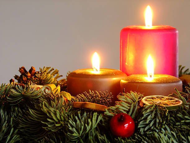 Drei brennende rosa Kerzen in einem Kranz aus Tannenzweigen mit einer roten Beere und Zitronenscheiben.