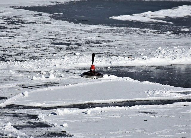 Eine rote und schwarze Eisangel ist auf der schneebedeckten Oberfläche in der Nähe eines zugefrorenen Sees platziert.