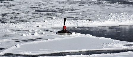 Ein rotes Eisangelgerät ruht auf einem zugefrorenen See, umgeben von Schnee und Eisbrocken.