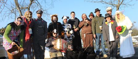 Eine Gruppe von Menschen in verschiedenen Kostümen posiert für ein Foto im Freien, wobei eine Person Akkordeon spielt und eine andere als Bär verkleidet ist.