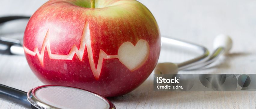 Ein roter Apfel mit einem Herz und einer EKG-Linie darauf. Daneben befindet sich ein Stethoskop. Credit: udra.