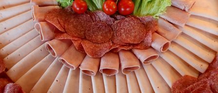 Ein Tablett mit verschiedenen geschnittenen Fleischsorten, einschließlich Salami, Schinken und anderen Wurstwaren, garniert mit grünem Salat und roten Kirschtomaten.