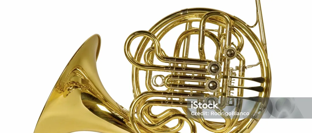 Ein goldenes Waldhorn wird vor einem weißen Hintergrund isoliert, wobei seine komplizierte Konstruktion und polierte Oberfläche zur Geltung kommt. Es ist ein Instrument von Schönheit und Komplexität.