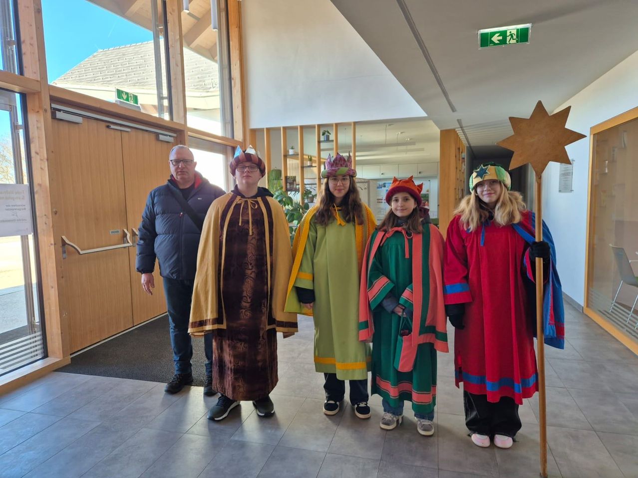 Fünf Personen in traditioneller Kleidung stehen in einem Flur. Ein Mann mit Brille steht neben einer Frau mit Krone und Stern.