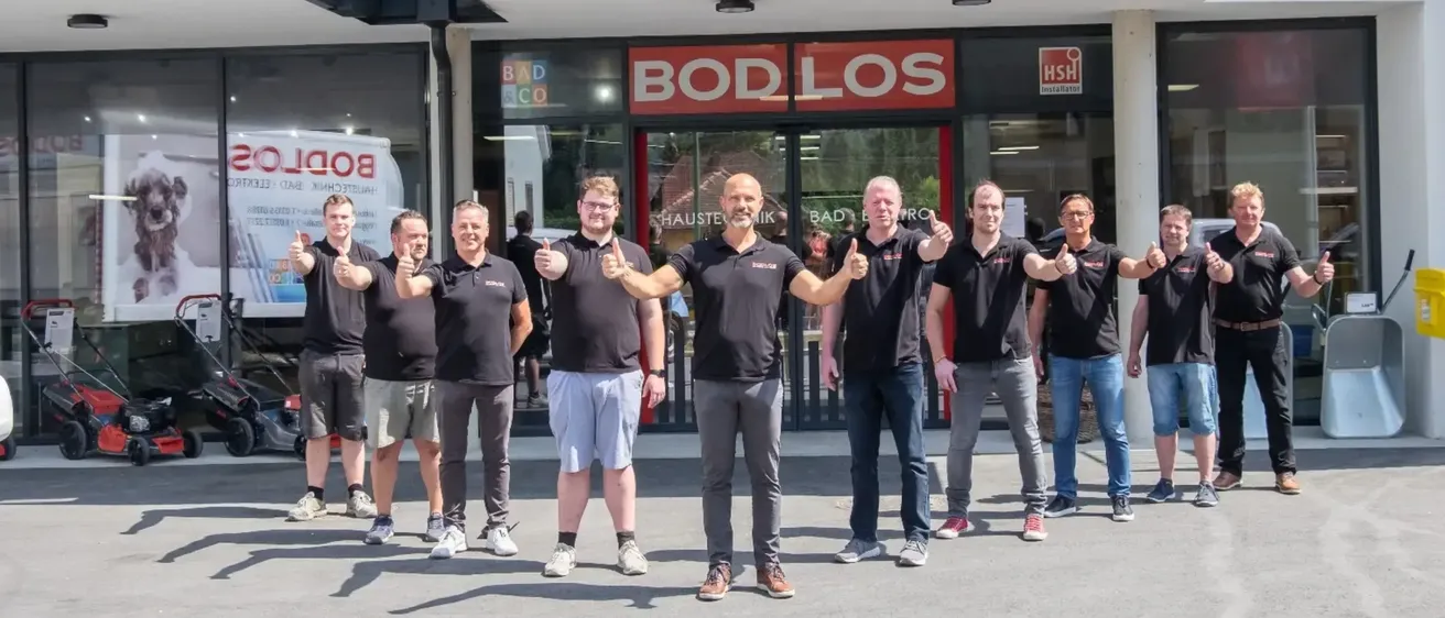 Eine Gruppe von Männern in schwarzen Shirts und Hosen posiert für ein Foto vor einem Geschäft namens Bod Los.