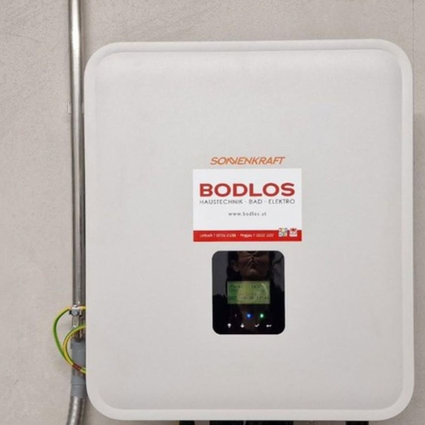 A white solar inverter by Bodlos is mounted on a wall with a digital display showing temperature and power.