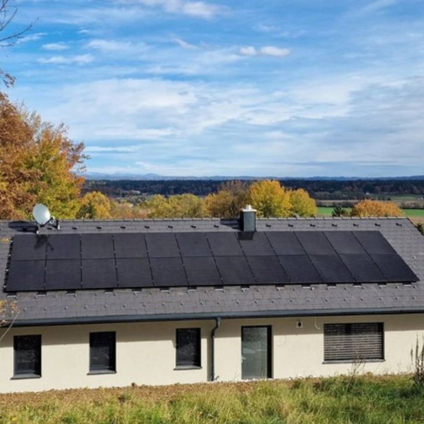 A house with a large solar panel array on its roof, surrounded by trees, under a partly cloudy sky.