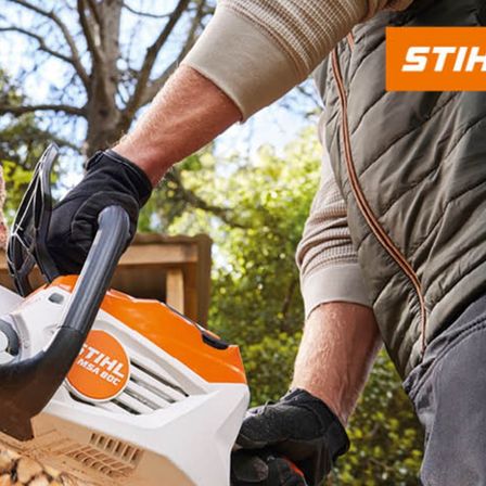 Eine Person mit Handschuhen hält eine orange-weiße STIHL-Kettensäge und schneidet Holz im Freien.