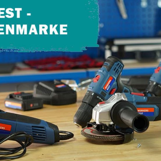 Eine Sammlung von blauen und schwarzen Elektrowerkzeugen liegt auf einer Holzoberfläche. Sie liegen auf einem blauen Metall-Aufbewahrungskasten.