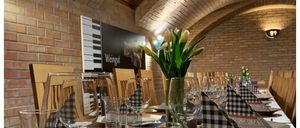 Ein Weinkeller für Sie, eine Veranstaltung im privaten Rahmen. Ein Tisch mit Weingläsern, Servietten und Tellern. Eine Ziegelwand mit Poster und Lampen.