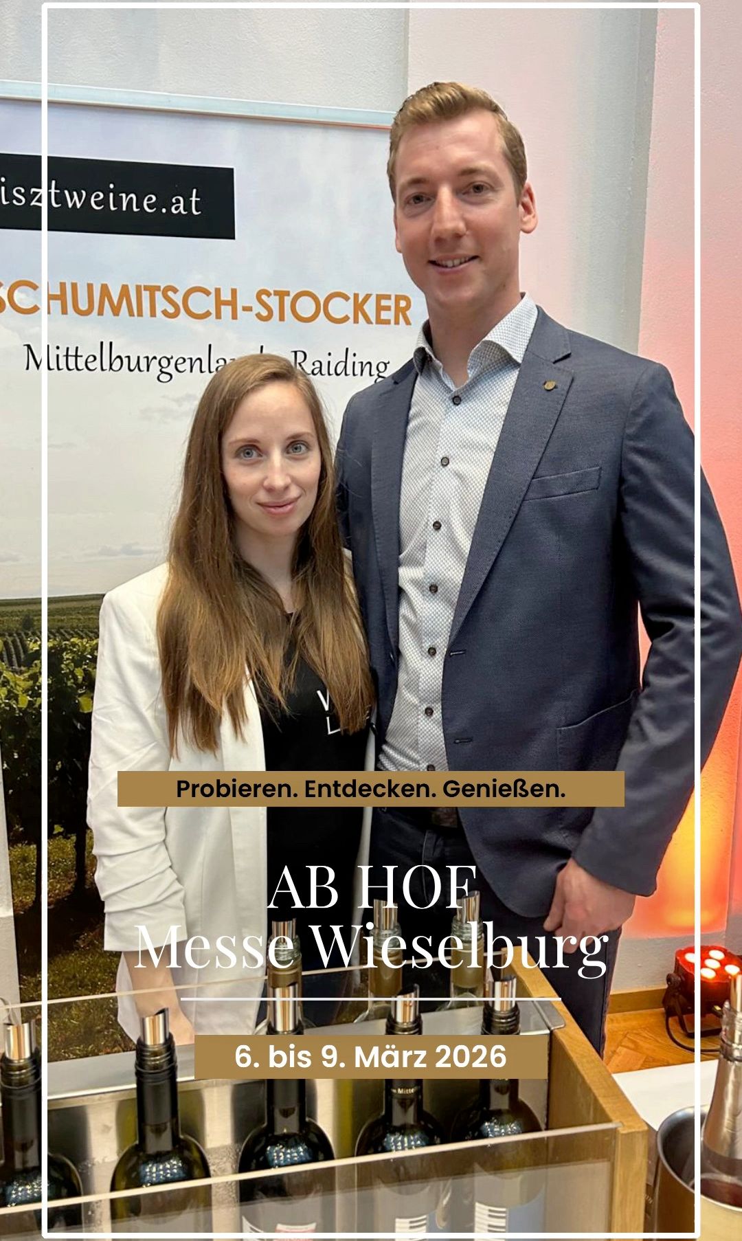 Two people stand close to each other in front of a vineyard backdrop, smiling for the camera. They are wearing formal attire. The woman is wearing a white blazer and the man is wearing a blue suit. A text overlay reads, 'Try. Discover. Enjoy.' and the name 'AB HOF Messe Wiesbaden' is displayed.