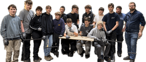 Eine Gruppe junger Männer steht und sitzt um einen Holztisch herum, alle tragen Handschuhe. Sie scheinen an einer Art manueller Aktivität beteiligt zu sein.