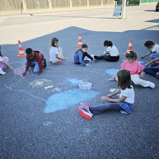 Kinder sitzen auf dem Boden und zeichnen mit Kreide. Sie tragen Freizeitkleidung und Turnschuhe. Einige halten Kreideboxen.