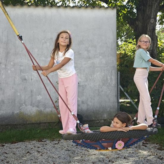 Drei junge Mädchen spielen auf einer Reifenschaukel im Freien. Ein Mädchen liegt, während die anderen beiden stehen.