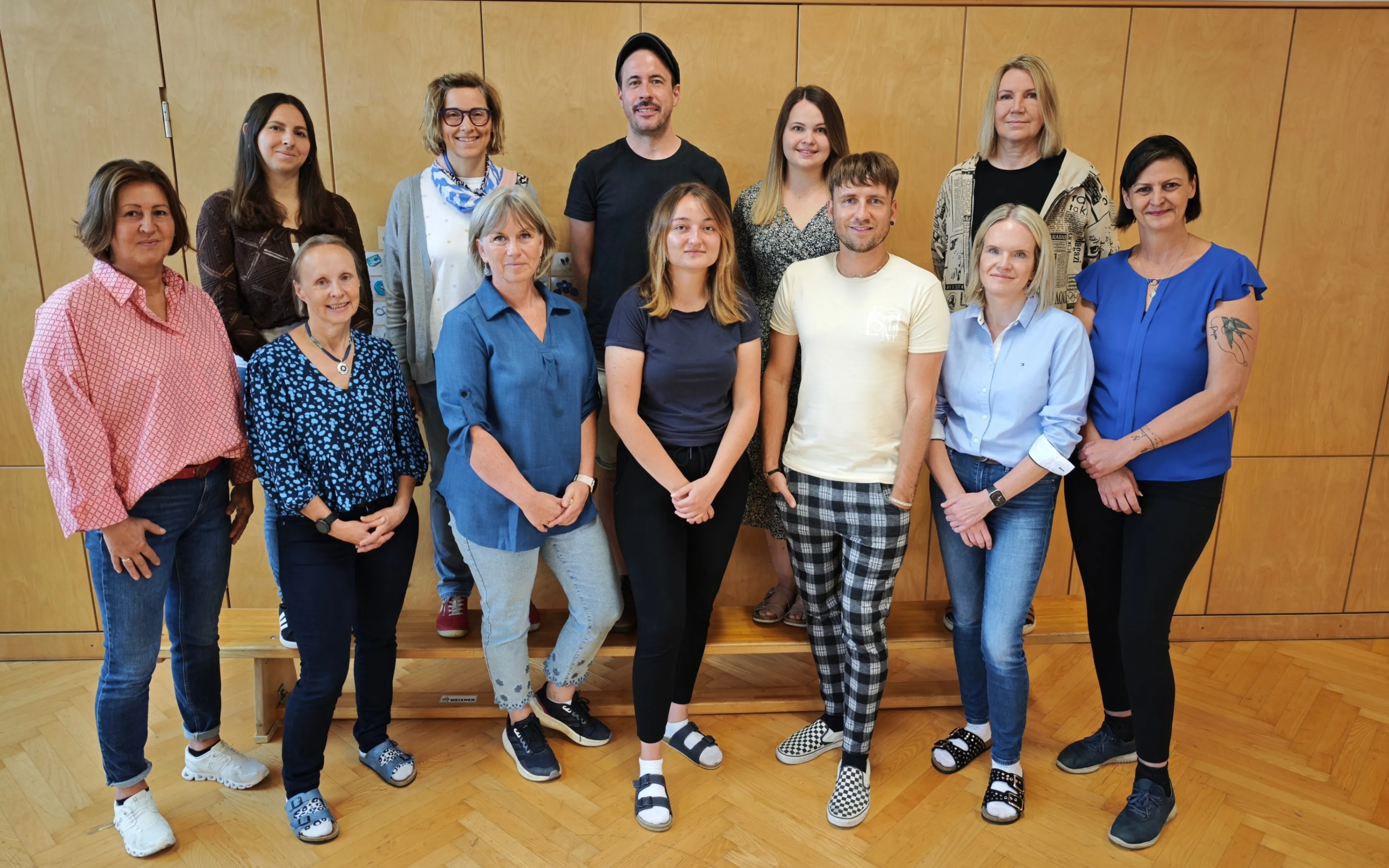 Eine Gruppe von Erwachsenen in lässiger Kleidung posiert für ein Foto in einem Raum mit Holzwänden.