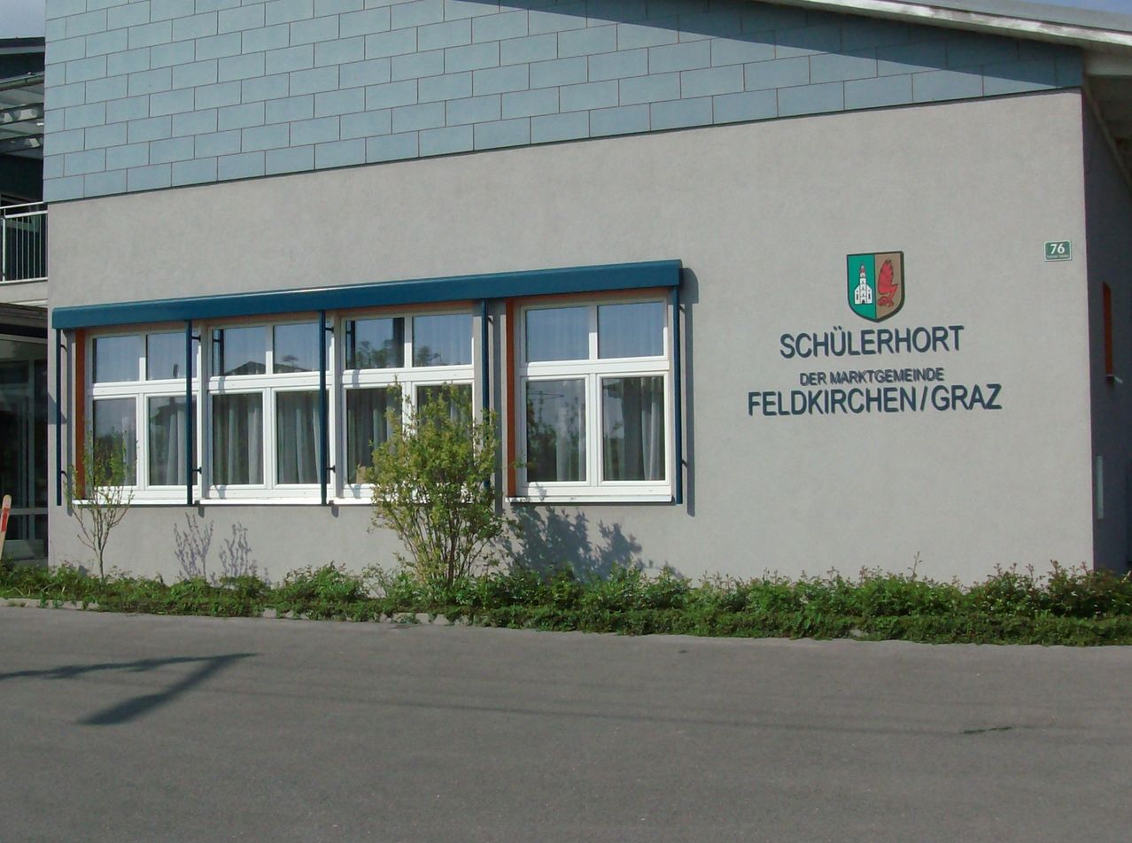 Vorderansicht eines Gebäudes mit blauem Dach, weißen Fenstern und einem Schild, das 'Schiilerhorp der Marktgemeinde Feldkirchen/O' liest.
