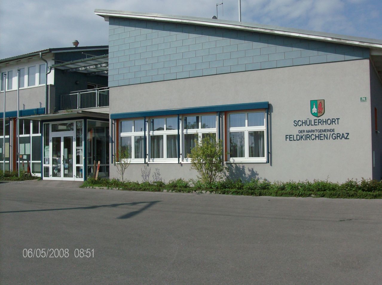 Vorderansicht eines Gebäudes mit blauem Dach, weißen Fenstern und einem Schild, das 'Schiilerhorp der Marktgemeinde Feldkirchen/O' liest.