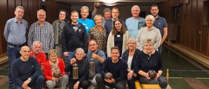 Eine Gruppe von Menschen posiert für ein Foto, hält Bowlingbälle in den Händen und trägt verschiedene Kleidungsstücke, in einer Bowlingbahn.