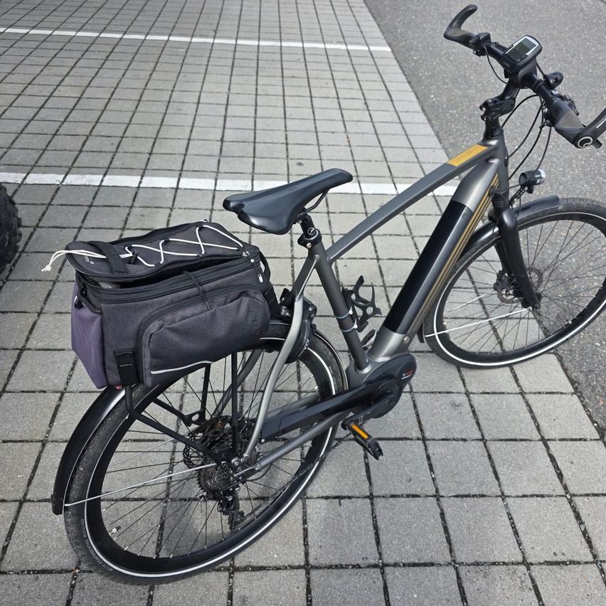 A black and yellow electric bicycle with a bag attached to the back is parked on a paved surface.