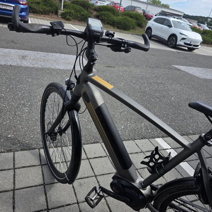 A close-up view of a modern electric bicycle with a digital display on the handlebars, parked on a paved sidewalk.
