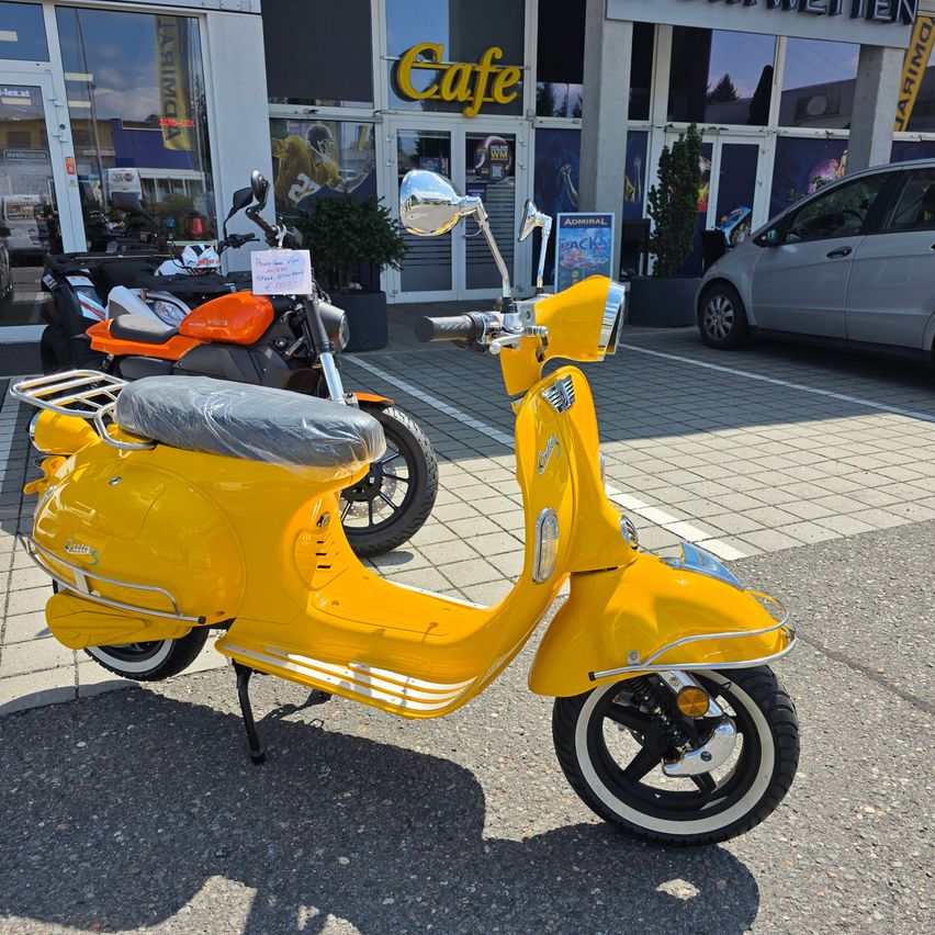 A bright yellow Vespa scooter is parked in front of a cafe, with an orange motorcycle and a silver car in the background.