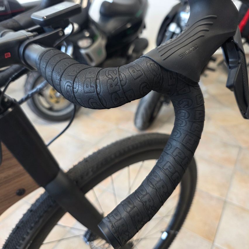 Nahaufnahme eines schwarzen Fahrradlenkers mit strukturiertem Griff und dem eingeprägten Wort 'PRO'. Der Lenker ist an einem Fahrrad mit schwarzem Reifen montiert.