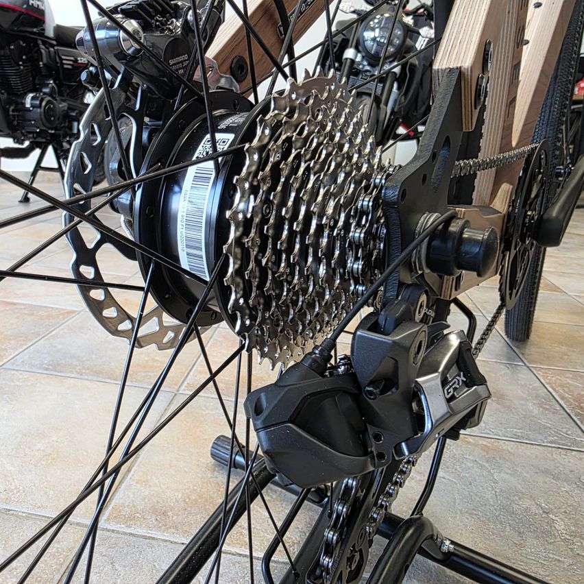 Eine Nahaufnahme des Hinterrads eines Fahrrads zeigt die Kette, Kettenräder und Bremskomponenten. Das Bild hebt die komplizierte Konstruktion und Technik des Fahrradantriebs hervor.