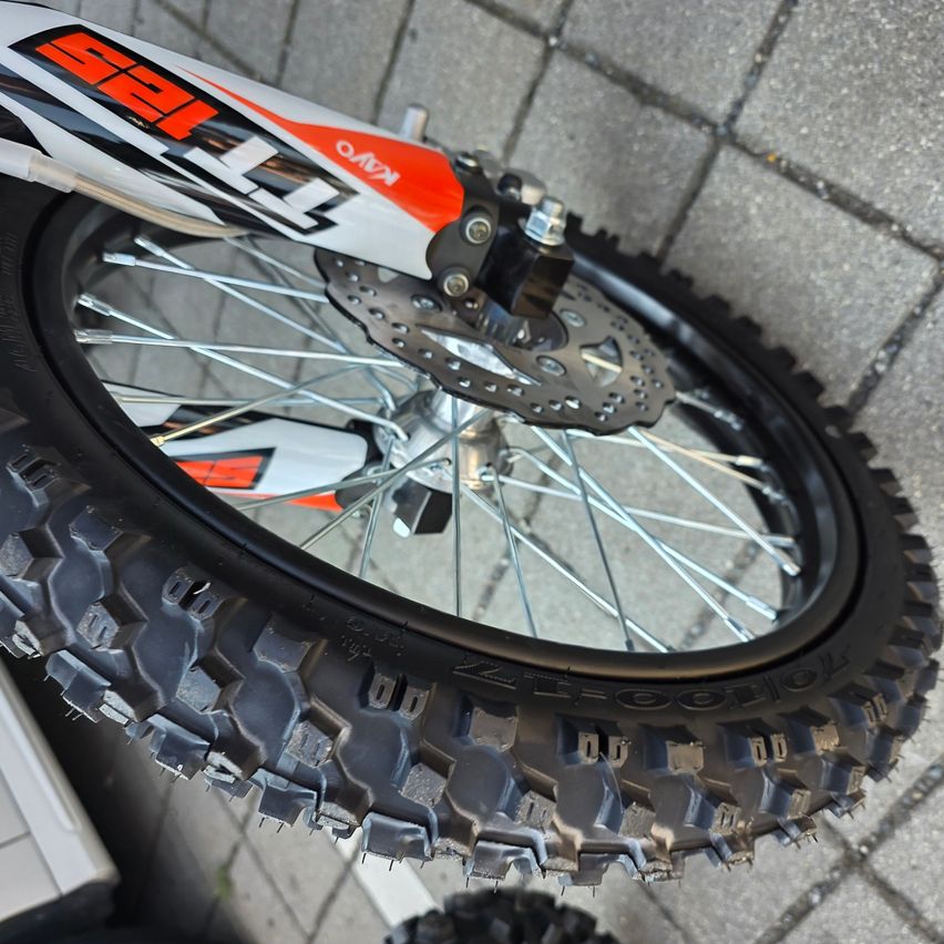 Nahaufnahme eines Motorradrads mit schwarzem Reifen und silbernen Speichen. Das Rad ist an einem Fahrrad mit weißem und orangefarbenem Rahmen montiert.