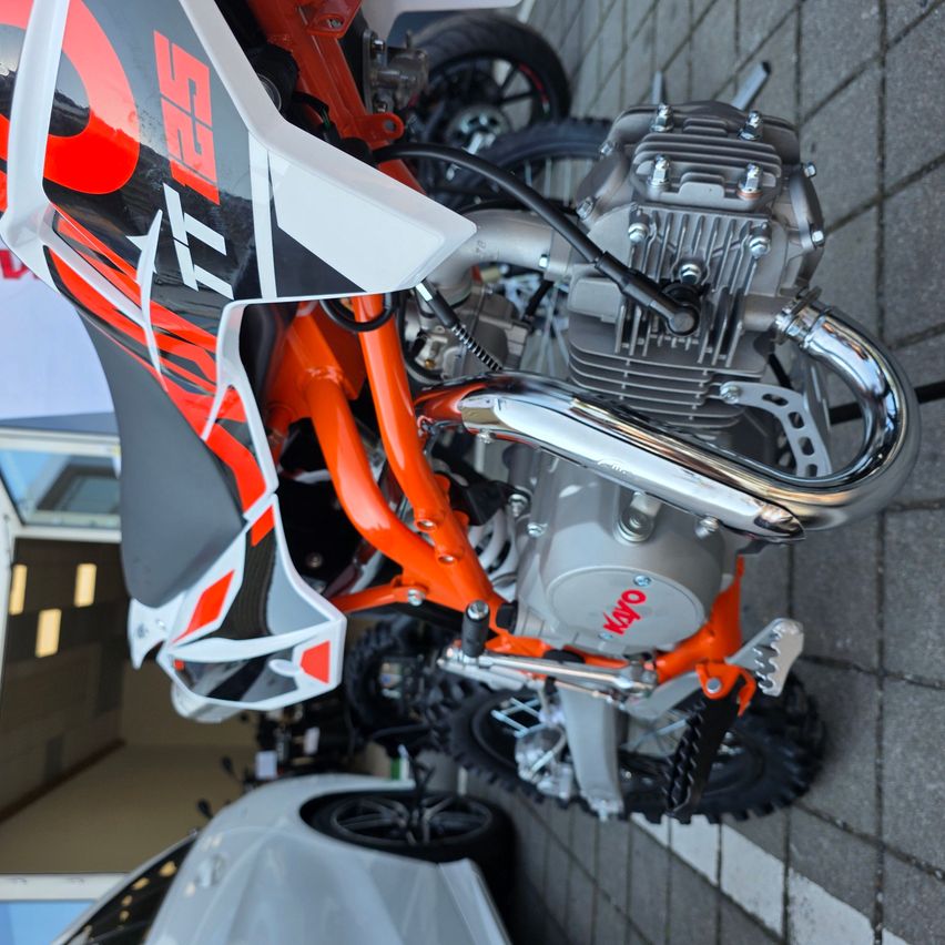 Ein Blick von oben auf ein kleines orange-schwarzes Motorrad mit dem Wort 'KTM' auf dem Motor. Das Motorrad steht auf einem Ziegelboden.