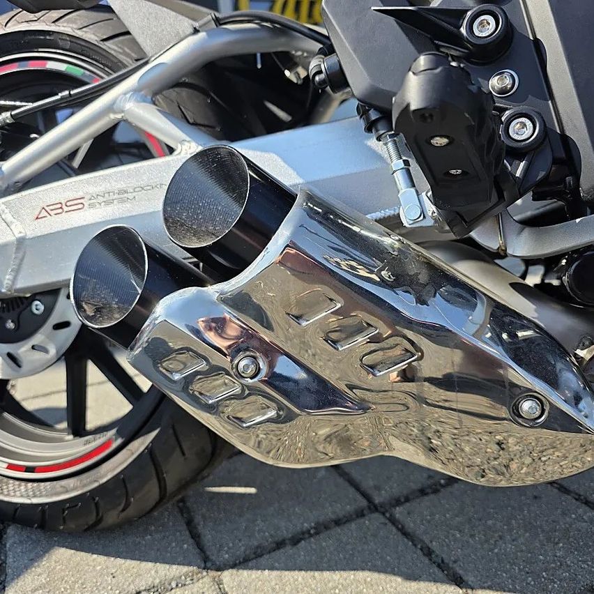 Nahaufnahme eines Motorrad-Auspuffsystems mit glänzendem Silberfinish und ABS-Antiblocksystem-Markierung.