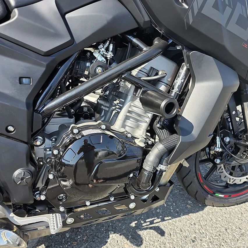 Eine Nahaufnahme des Motorradmotors, die den Motorblock, das Auspuffsystem und verschiedene mechanische Teile zeigt.