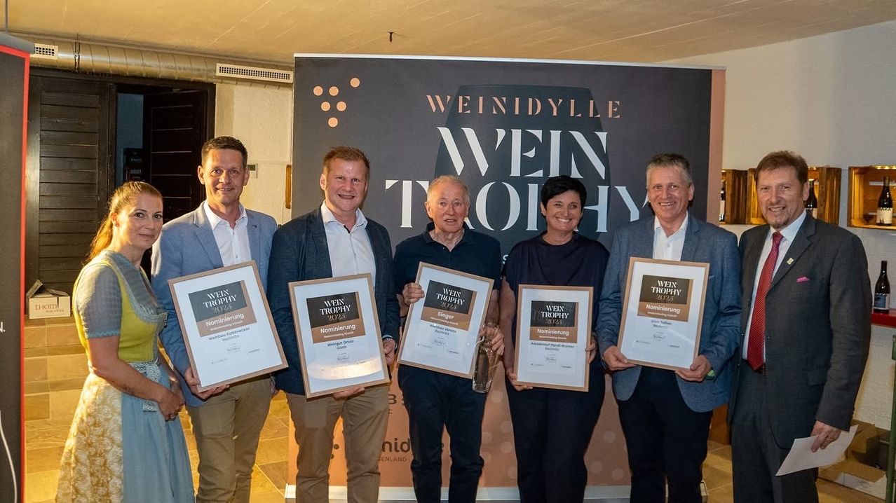 Fünf Personen stehen vor einem Banner mit dem Text Wein Trophy. Sie halten alle Auszeichnungen in den Händen.